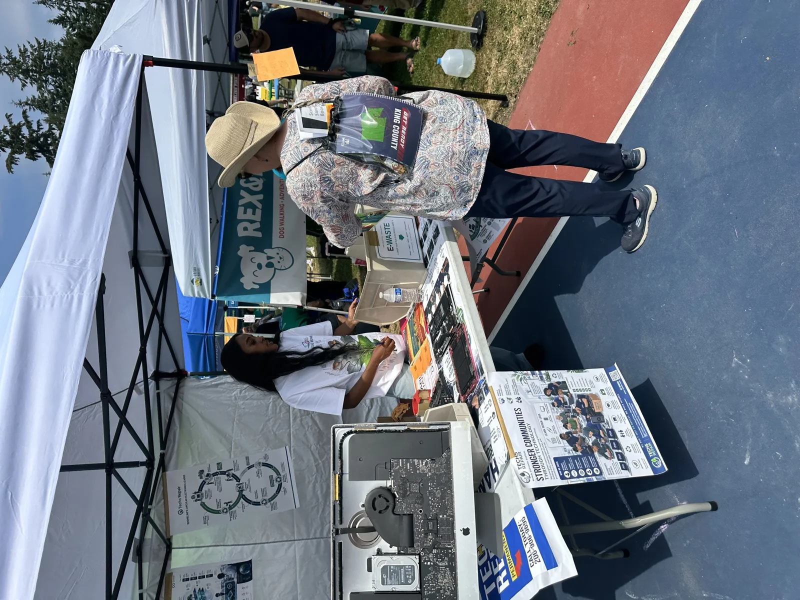 Techs Repair outreach booth with disassembled iMac and e-waste collection box at a community event